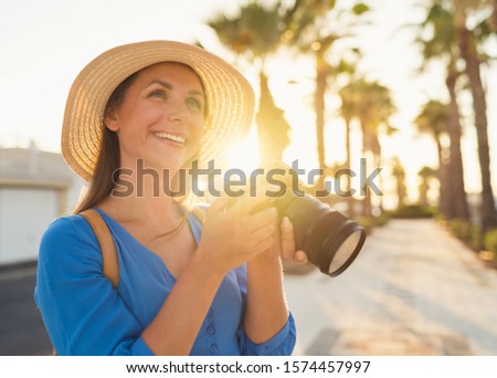 Happy photographer tourist woman taking photos with camera in a beautiful tropical landscape at sunset