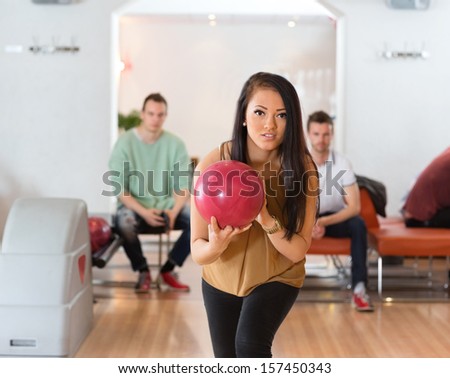 Young woman bowling with friends in background at club