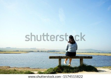 Young Asian woman is sitting alone on the bench near the sea on a sunny day while travelling.
