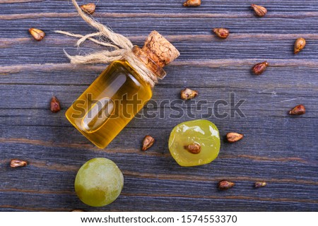 Bottle with grape oil and grape seeds on a wooden table.