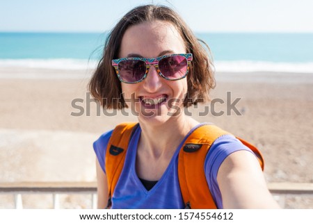 A girl takes a selfie on the waterfront. A woman walks through the resort town and takes pictures. Brunette travels around the Turkish city. Photo on the background of the sea and mountains.