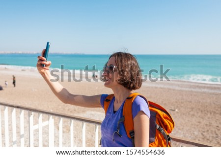 A girl takes a selfie on the waterfront. A woman walks through the resort town and takes pictures. Brunette travels around the Turkish city. Photo on the background of the sea and mountains.