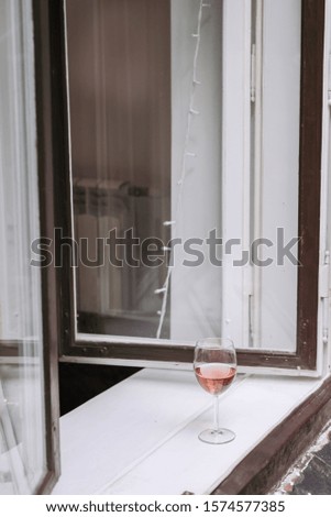 Glass of rose wine is standing on windowsill. Lifestyle view.