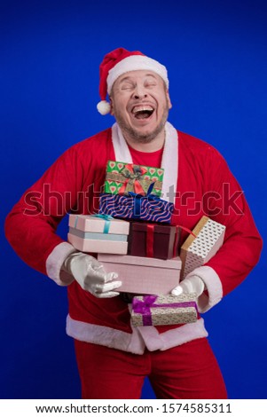 Santa Claus holds gift boxes in his hands and poses on a blue background