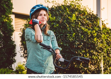 Portrait Of A Cheerful Girl Holding Mobile Phone. Happy smiling student using bike sharing app on smart phone outdoor. City lifestyle stylish hipster girl with bike using smartphone app in street.