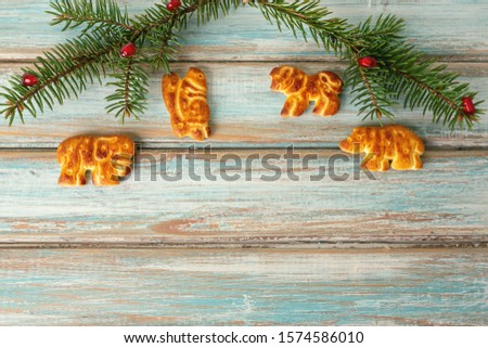 New year or Christmas background: two spruce branches decorated with red berries and cookies in the form of various animals on a blue background.