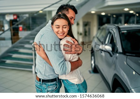 The successful visit to the dealership. Happy young couple happy hug that chooses and buying a new car for the family.