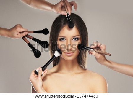 Studio photo of make-up process over grey background (concept with many hands)