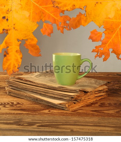 Cup of tea with autumn leaves reflection on newspaper on wood 