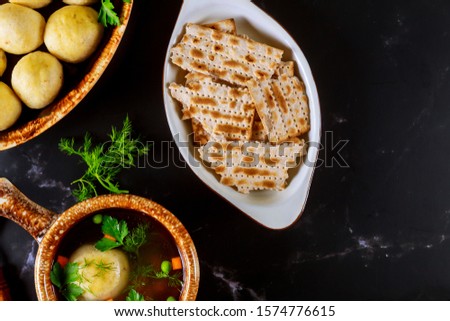 Bowl of Jewish matzoh balls soup with matzos on black background.