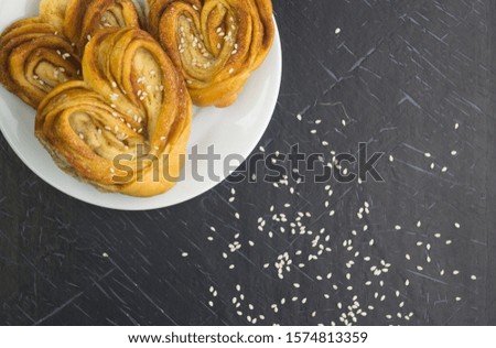 
homemade cinnamon rolls and sesame seeds laid out on a white plate standing on a black wooden board Flat lay
