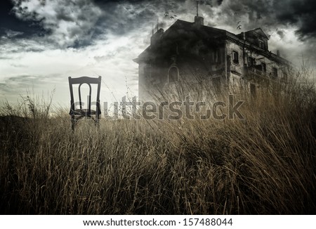 Abandoned chair out in a field facing a haunted house 