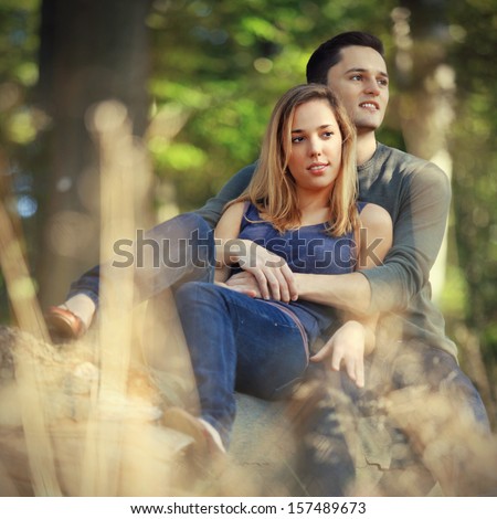 loving couple holding each other sitting on a tree trunk on a romantic date in the forest