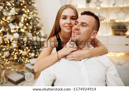 couple in love kisses and hugs on the sofa near the Christmas tree lights. New year's night.Christmas. black dress and white shirt, jewelry