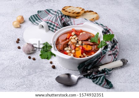 Stewed beans with sausages and vegetables in a ceramic dish. Selective focus.