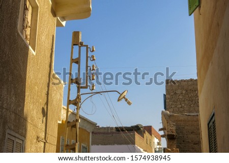 Simple street light in Marsa Alam. Curious and funny street lamp. High poles with lanterns on top, street lamp along the road in Egypt. White tin cover above sticking out bulb.
