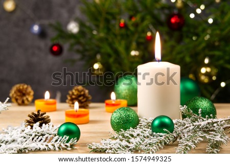 Burning candles and christmas decorations. Green balls for Christmas tree and fir twig on wooden floor with bokeh background. Copy space