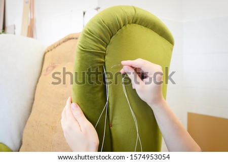 Making new upholstery on old armchair. Green velvet fabric. Restoration of old chair. Woman hands, working in upholstery workshop. Repairing old furniture. Hand sewing fabric. Royalty-Free Stock Photo #1574953054
