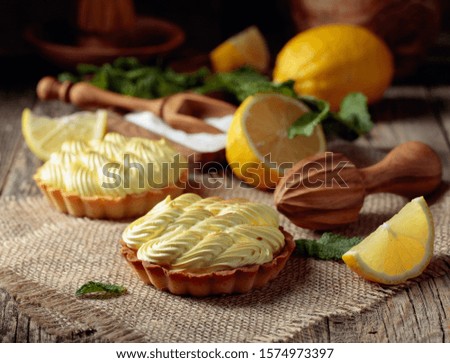 Tartlets with lemon cream and mint on a old wooden table. Homemade desserts with ingredients and wooden kitchen utensils. 