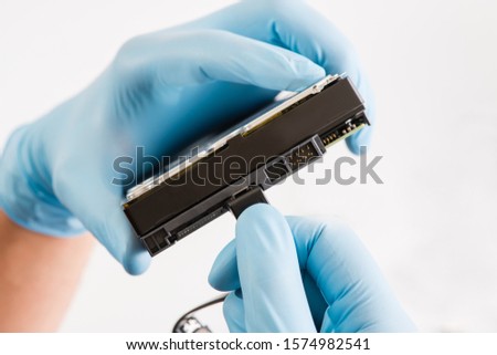 Repairman hand in blue runnber glove holds computer hard drive disk with green chip. white background.