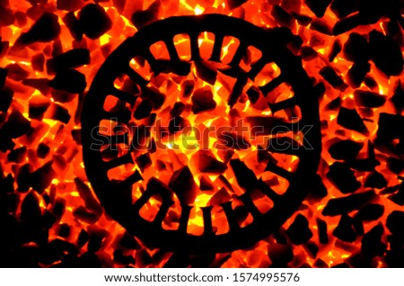 
An iron disk with holes and slots lies on a burning corner of anthracite, as a background.