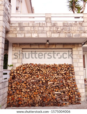 Large pile of dry chopped wood to prepare for the cold winter, laying outside in front of a home garage.
