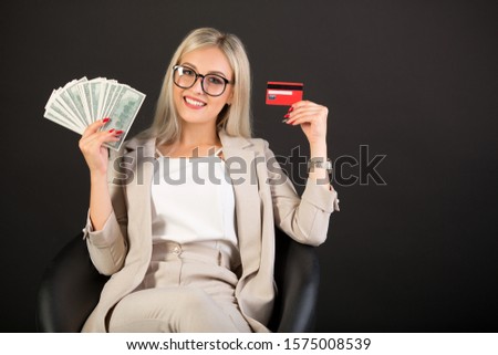 beautiful young woman in a suit on a black background with a credit card and dollars in hands