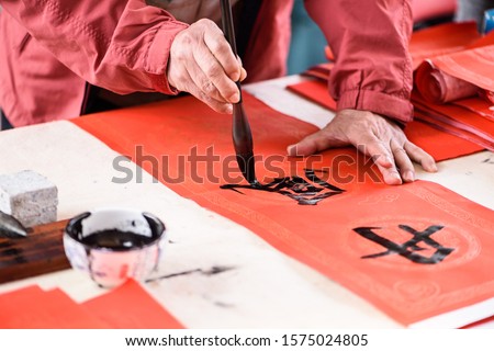 Man who is writing Spring Festival couplets, the Chinese characters "Dan Feng" on the red paper couplet meas "red wind" Royalty-Free Stock Photo #1575024805