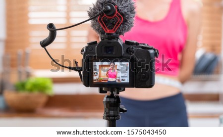 Young Asian blogger holding measuring tape around her wais while recording video on camera at home.media influencer reviewing and marketing concept