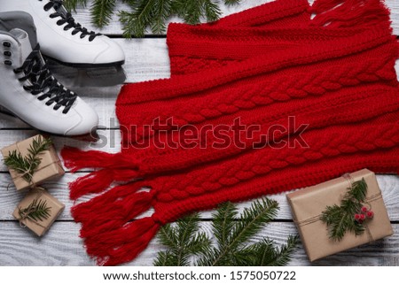 Christmas holidays activitybackground. Top view of Christmas tree branches with woman skates and bright red knitted scarf with wrapped gift boxes