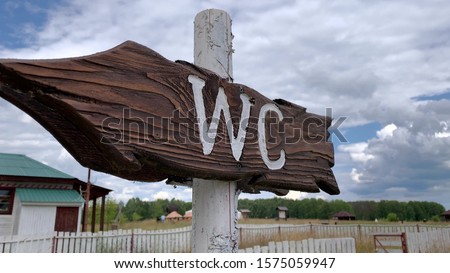 An outdoor wooden arrow signboard WC, public restroom sign in a countryside park.