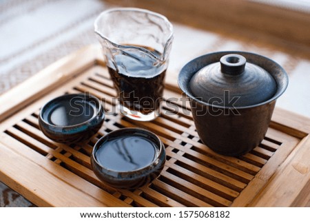 Chinese tea ceremony. Cups filled with black tea and a transparent glass are on the board. Close-up