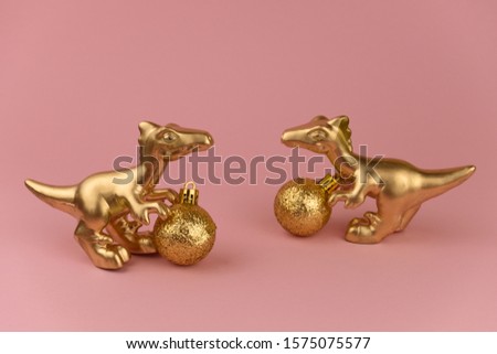 golden dinosaurs toy with golden christmas ball on a pastel pink background, trendy modern christmas card with copy space