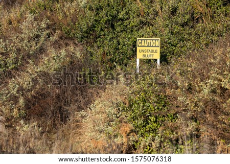 "Caution. Unstable Bluff" sign on an eroding coastal hillside