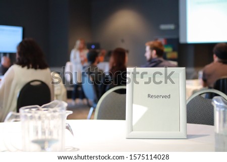 A Classy reserved table sign with a water drinking glass at a business event for entrepreneurs. There is shallow depth of field in photo.