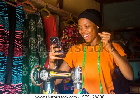 young african woman who is a tailor feeling excited and happy and jubilant while viewing content on her mobile phone Royalty-Free Stock Photo #1575128608