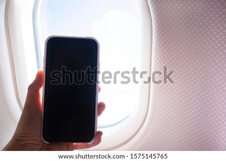 mock up Image of female hand holding smartphone with a blank desktop screen next to an airplane window. Black screen mobile phone, travel