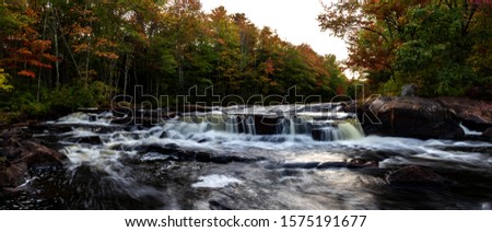 Mousam River at dusk in Sanford, Maine. Panoramic foliage and long exposure over rocks.