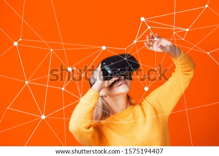 Computer game player uses virtual reality. A young woman in a VR helmet, have a fun, portrait on a yellow background. touching something by hand. entering the simulation