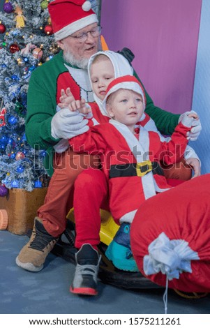 Dad, Happy children are dressed in festive costume of Santa Claus and snowman, carrying decorated Christmas tree with balls and garlands on yellow car, accompanied by rocking horse. Christmas Eve