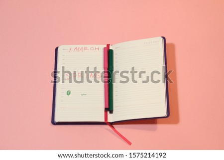 Paper notebook and  colorful pen on pages with 1 march, spring text on pink  background