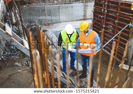Men in hardhat and yellow and orange jacket posing on building site