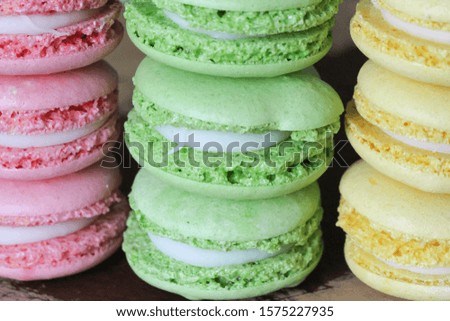 Close-up view of macarons (or french macarons) in a variety of colors (pink, green and yellow) with lemon cream on wooden cutting board. Pastries lies on top of each other according to their color.