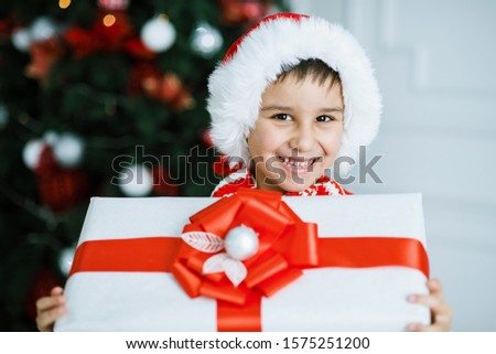 Happy excited child holding christmas gift box. Boy giving a Christmas present in decorated room. christmas and people concept. New Year Happy holidays. kid satisfied with present.