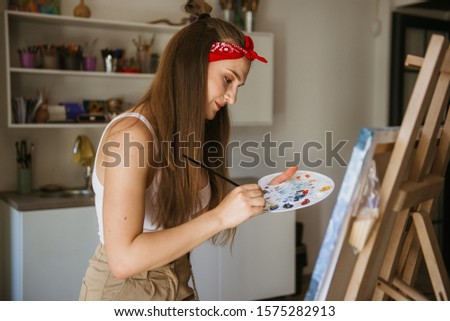 young beautiful girl paints a picture on an easel
