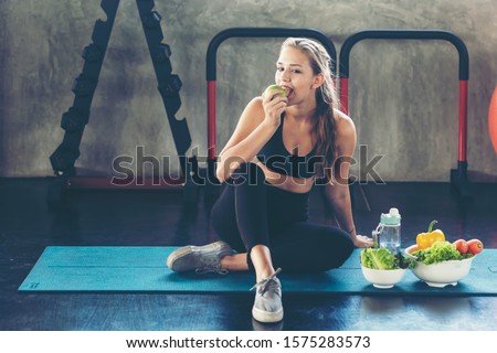 Lifestyle women eating green apple and fresh salad after exercise  at the gym workout for healthy care and body slim.  Diet and Healthy sport Concept Royalty-Free Stock Photo #1575283573