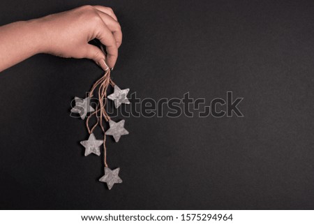 Female hand holding wooden stars with rope, flat lay over black background
