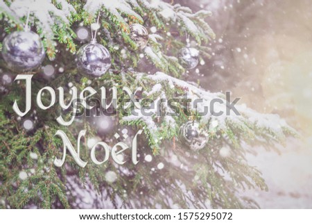 "Joyeux Noël" means "Merry Christmas" in French. Blurred background of beautiful Christmas tree in snowfall and bright silver lights, toys. Bokeh. Happy New Year! Greeting postcard France Paris.