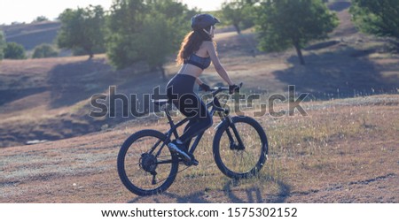 Girl on a mountain bike on offroad, beautiful portrait of a cyclist at sunset, Fitness girl rides a modern carbon fiber mountain bike in sportswear. The girl looks towards freedom and relaxation.