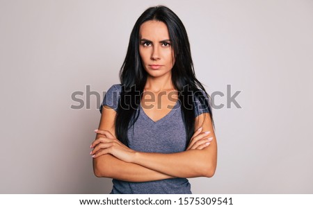 Don't mess with me! Close-up photo of a beautiful serious woman with long black hair, who is standing in front of the camera with folded arms and looking in the camera.